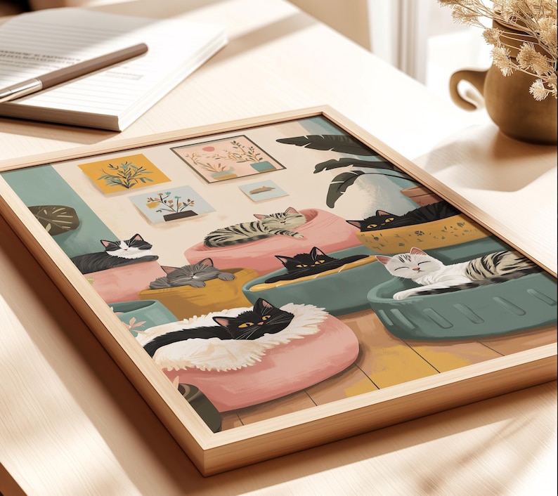 May include: A framed art print featuring a whimsical illustration of cats lounging in colorful beds. The artwork showcases various cat breeds, including black, gray, and tabby cats, in a cozy indoor setting. The print is set in a light wood frame.