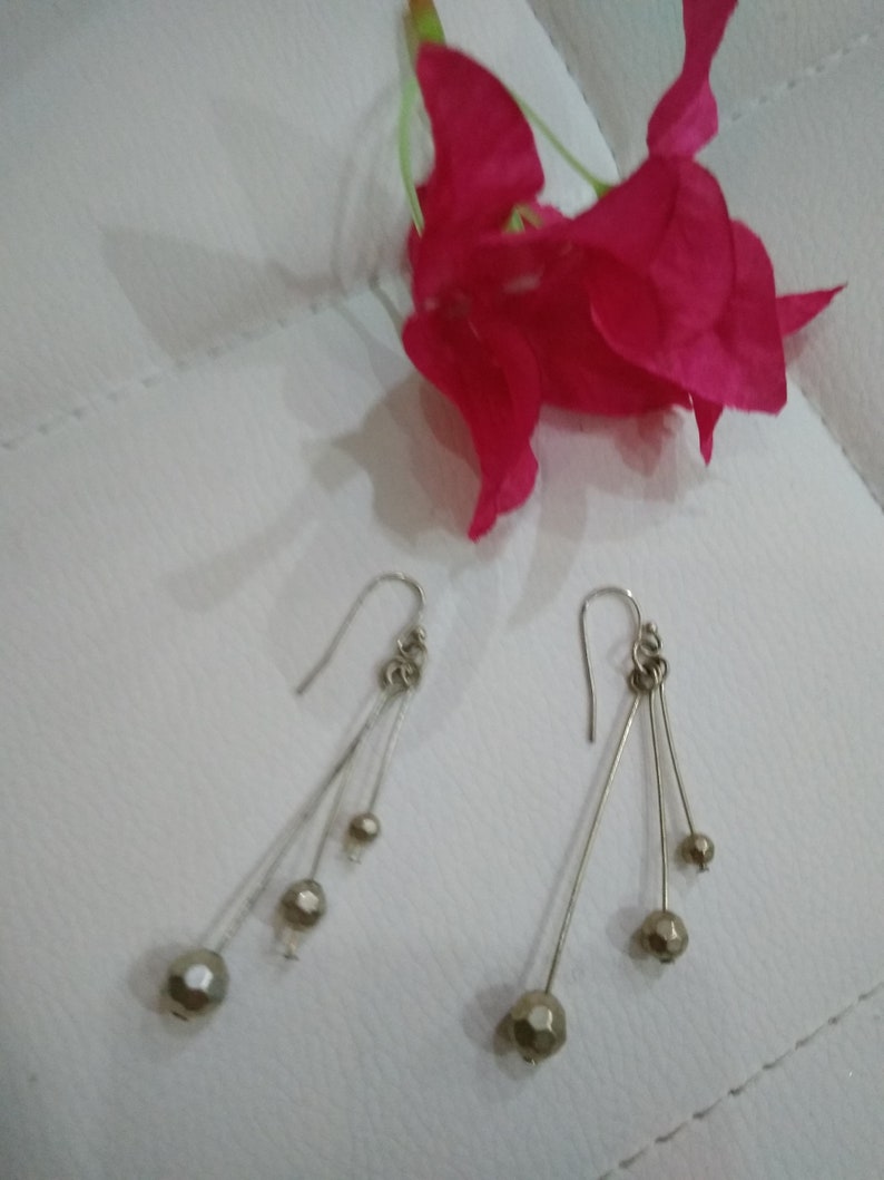 以下が含まれることがあります： 3つの丸いファセットカットビーズがついた、シルバーのドロップイヤリングのペア