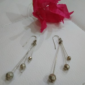 以下が含まれることがあります： 銀製のドロップイヤリングのペア。各イヤリングには、金色のファセットカットの丸いビーズが3つ付いています。