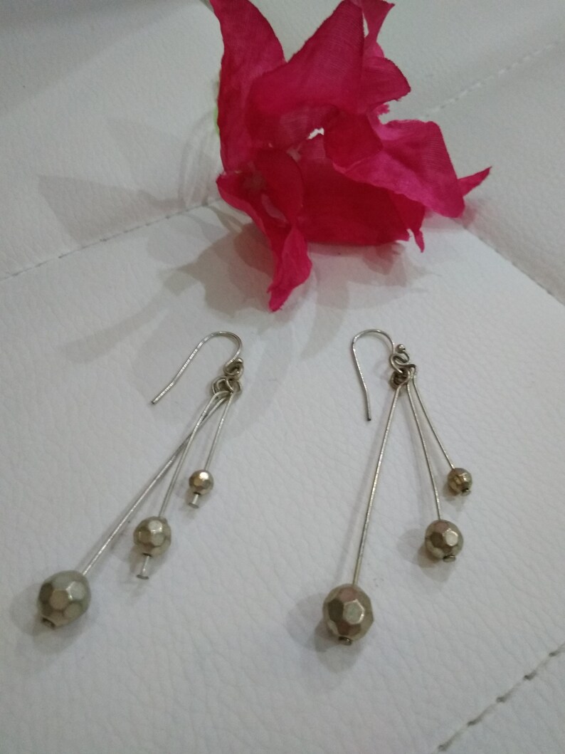 以下が含まれることがあります： 銀製のドロップイヤリングのペア。各イヤリングには、金色のファセットカットの丸いビーズが3つ付いています。