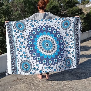 May include: A white cotton tapestry with a blue and white mandala design featuring multiple evil eye symbols. The tapestry has a fringed edge.