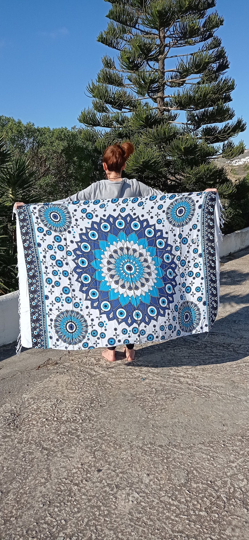 May include: A white cotton tapestry with a blue and white mandala design featuring multiple evil eye symbols. The tapestry has a fringed edge.