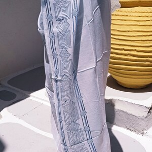 May include: White cotton sarong with a blue geometric pattern. The sarong is tied around the waist and has a long, flowing skirt.