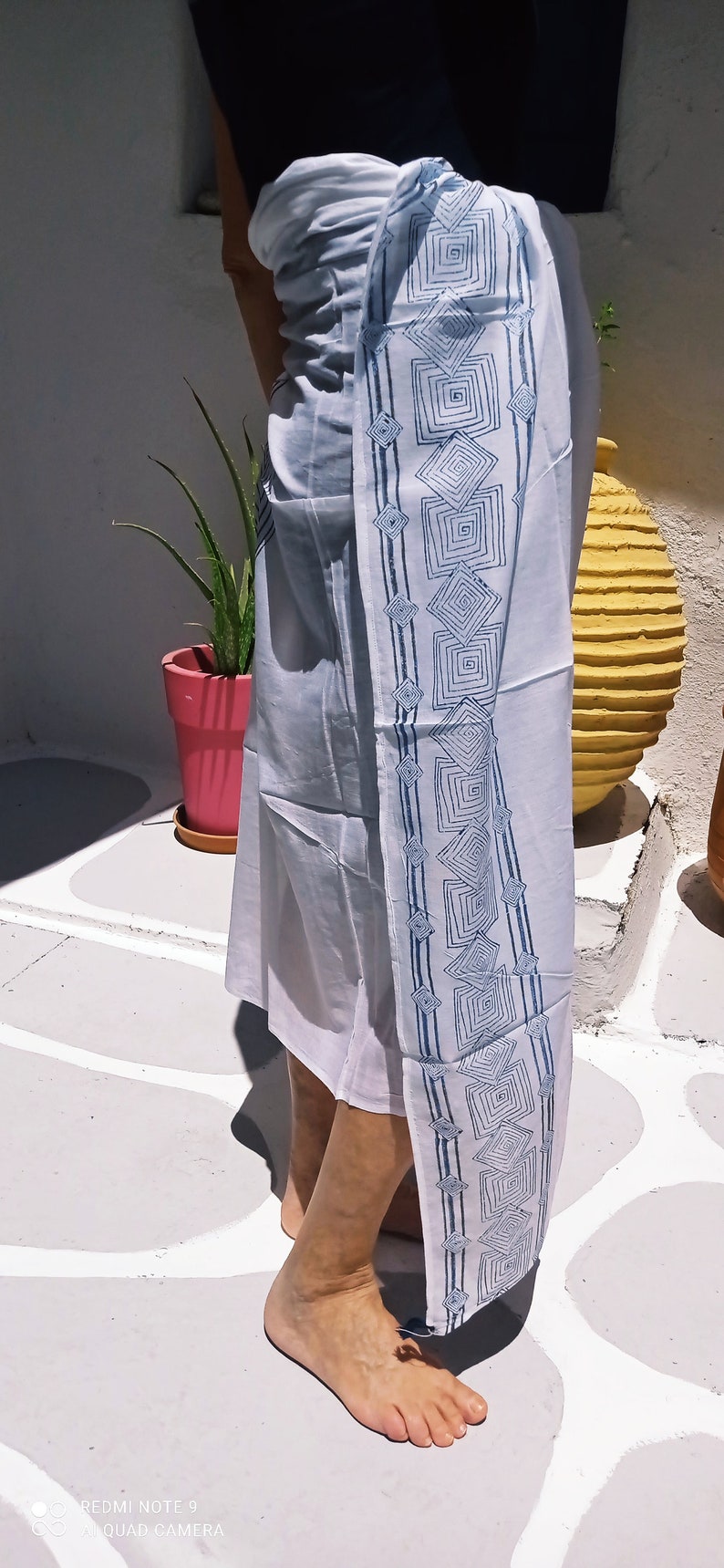 May include: A white sarong with a blue geometric pattern. The sarong is tied around the waist and the pattern is visible on the side.