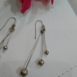 以下が含まれることがあります： 複数の小さなファセットカットビーズがぶら下がった、銀製のドロップイヤリングのペアです。