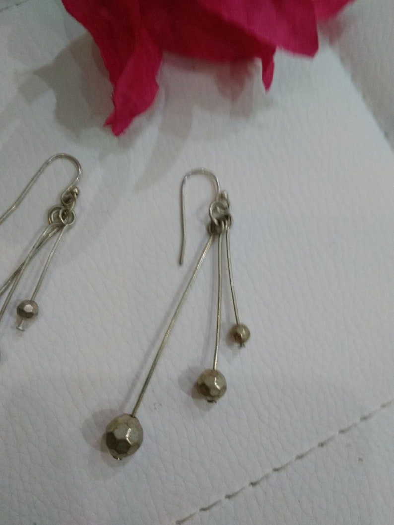 以下が含まれることがあります： 複数の小さなファセットカットビーズがぶら下がった、銀製のドロップイヤリングのペアです。