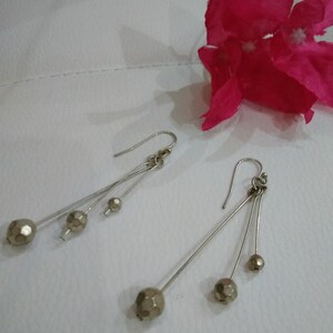 以下が含まれることがあります： 銀製のドロップイヤリングのペア。各イヤリングには、小さなファセットカットのゴールドトーンのビーズが3つ付いています。