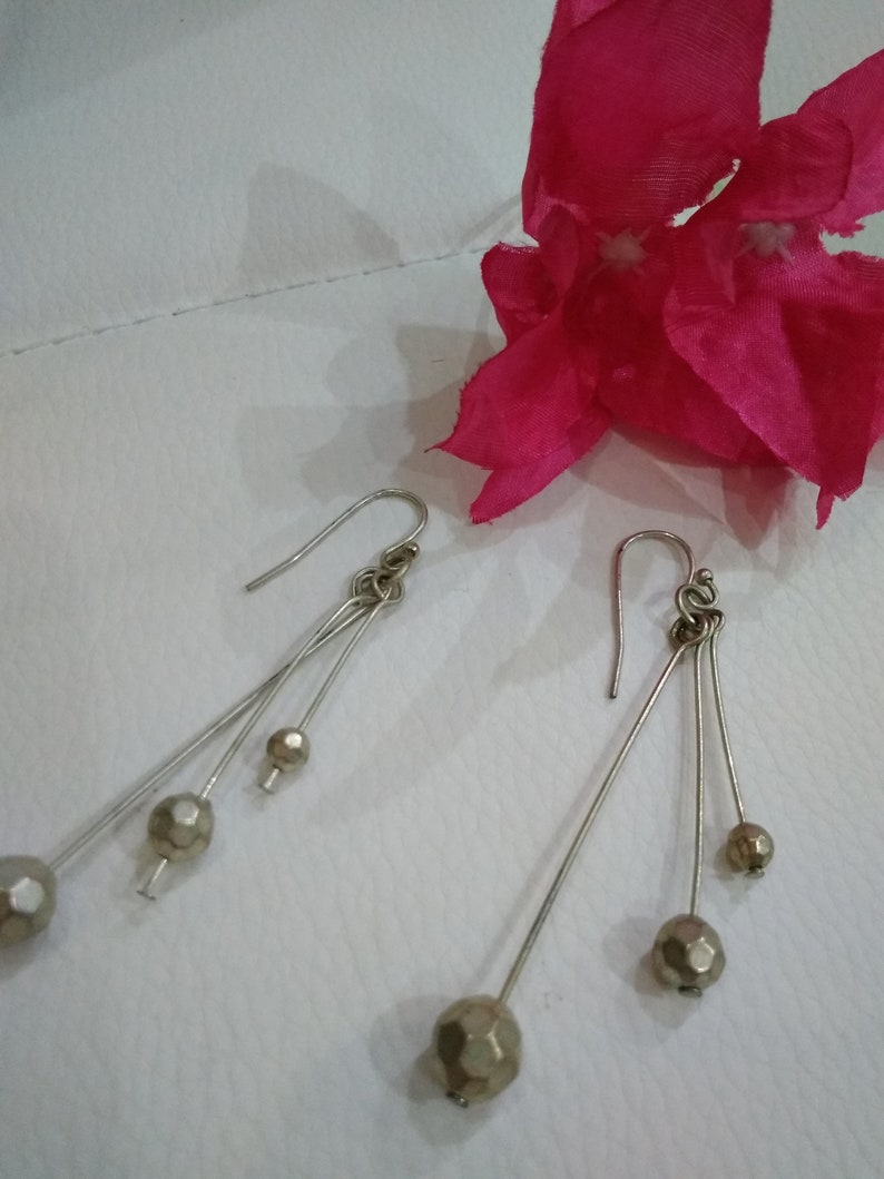 以下が含まれることがあります： 3つの丸いファセットカットビーズがついた、シルバーのドロップイヤリングのペアです。