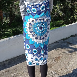 May include: A woman wearing a grey sweater and black leggings with a blue and white patterned sarong tied around her waist. The sarong features a large blue eye design.
