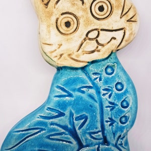 May include: A ceramic cat ornament with a blue and white glaze. The cat has a white face with brown eyes and a brown nose. The cat is wearing a blue coat with a floral pattern.