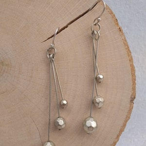 以下が含まれることがあります： 細いワイヤーから複数の幾何学的なビーズがぶら下がった、銀製のドロップイヤリングのペアです。