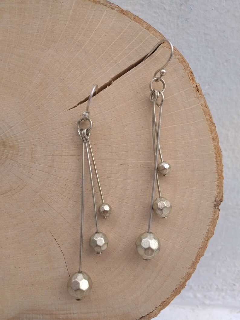 以下が含まれることがあります： 細いワイヤーから複数の幾何学的なビーズがぶら下がった、銀製のドロップイヤリングのペアです。