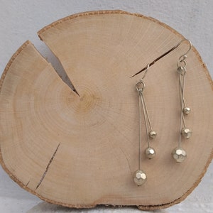 以下が含まれることがあります： 細いワイヤーから複数の幾何学的なビーズがぶら下がった、ゴールドトーンのドロップイヤリングのペアです。