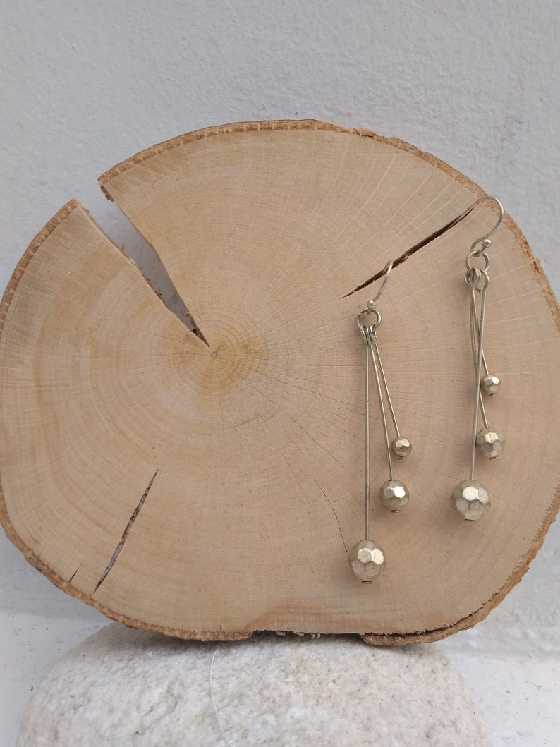 以下が含まれることがあります： 細いワイヤーから複数の幾何学的なビーズがぶら下がった、ゴールドトーンのドロップイヤリングのペアです。