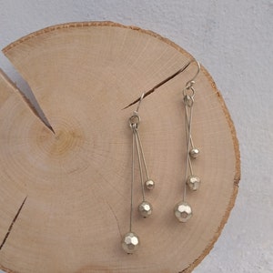 以下が含まれることがあります： 細い銀色のワイヤーから複数の幾何学的なビーズがぶら下がった、銀色のドロップイヤリングのペアです。