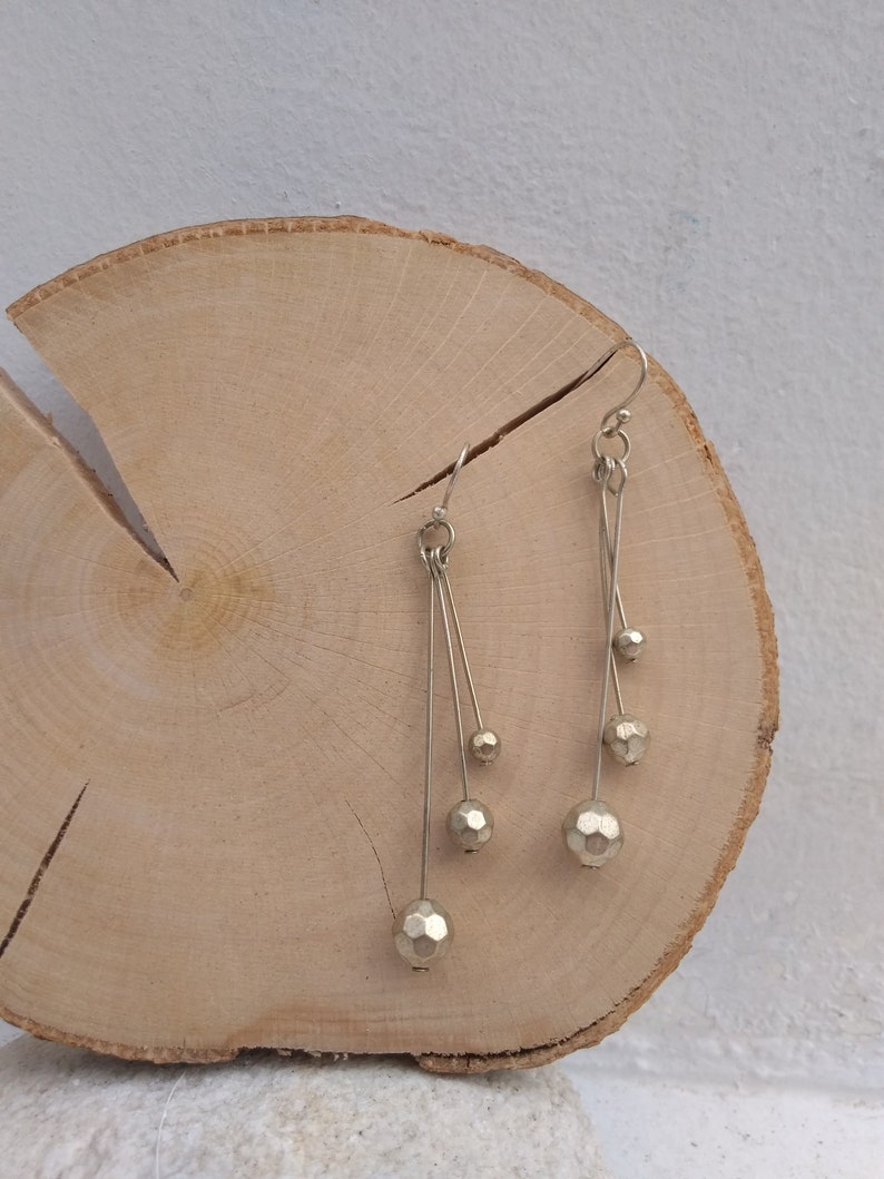 以下が含まれることがあります： 細い銀色のワイヤーから複数の幾何学的なビーズがぶら下がった、銀色のドロップイヤリングのペアです。