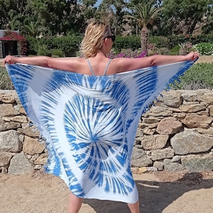 May include: A person wearing a white and blue tie-dye sarong with a fringe trim. The sarong is being held out in front of the person, creating a circular shape.