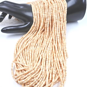 May include: A large collection of light beige, disc-shaped beads strung on multiple thin white threads. The beads have a natural, textured appearance with subtle variations in color and tone, arranged in long, parallel vertical strands.