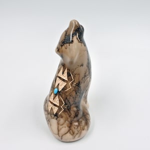 May include: A small ceramic wolf figurine with brown and black marbling and a turquoise stone inlay. The wolf is howling with its head tilted back.