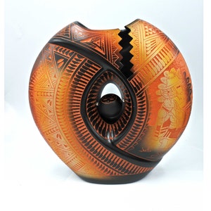 May include: A black and orange ceramic vase with a unique, abstract design. The vase is split in half, with a hole in the center. The vase is decorated with geometric patterns and a stylized figure.