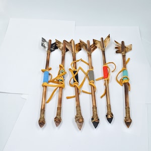 May include: Six wooden arrows with fletching and colorful bead accents. The arrows are tied with leather thongs and have a variety of arrowhead styles.