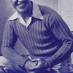 May include: A man wearing a blue knitted sweater with a v-neck. The sweater has a ribbed texture.