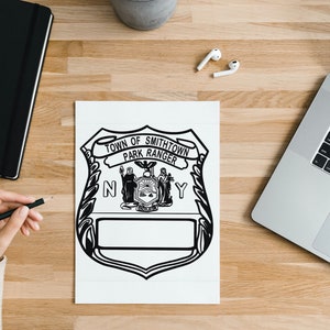 Puede incluir: Ilustración en blanco y negro de una insignia para un guardabosques del pueblo de Smithtown. La insignia presenta el sello del estado de Nueva York y el texto "Town of Smithtown Park Ranger" en una pancarta.