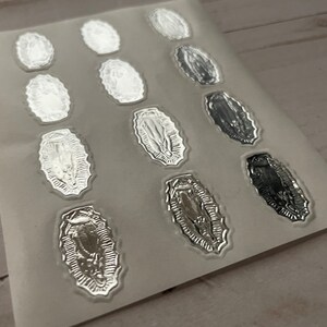 May include: A sheet of silver foil stickers featuring an image of the Virgin Mary. The stickers are oval shaped and have a detailed design.