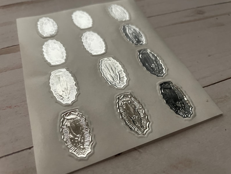 May include: A sheet of silver foil stickers featuring an image of the Virgin Mary. The stickers are oval shaped and have a detailed design.