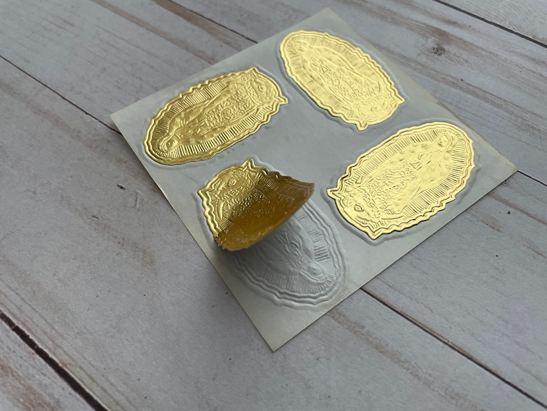 May include: A sheet of gold foil stickers featuring an image of the Virgin Mary. The stickers are oval shaped and have a raised, textured design.