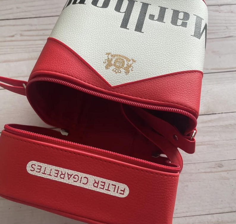 May include: A red and white cigarette-shaped bag with a zipper closure. The bag has the word "Marlboro" printed on it in black. The bottom of the bag reads "FILTER CIGARETTES".