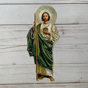 Könnte beinhalten: Ein religiöses Bild eines Mannes mit einem Heiligenschein, der einen Stab und ein Herz hält. Er trägt eine grüne Robe und eine weiße Tunika. Das Bild ist auf einem Holzgrund.