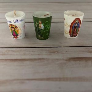 May include: Three small votive candles with religious imagery. One candle has the text "Ame Mucho" and an image of the Virgin Mary. Another features an image of a saint on a green background. The third candle has an image of the Virgin Mary.