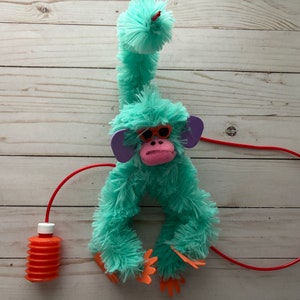 May include: A turquoise plush monkey toy with pink ears and orange hands. The monkey has a red string attached to its tail and a red pump bottle.