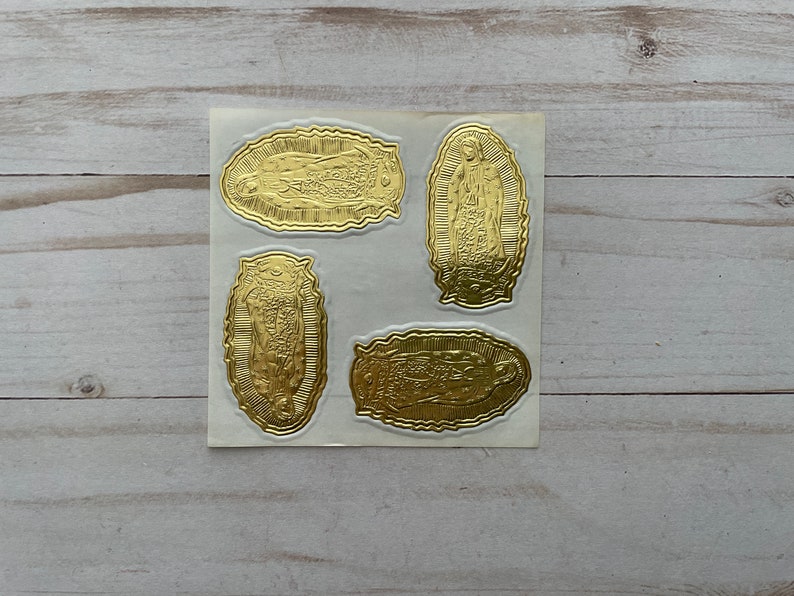 May include: Four gold foil stickers featuring an image of the Virgin Mary. The stickers are oval shaped and have a white background.
