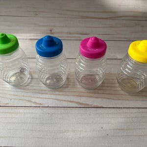 May include: Four clear plastic bottles with colourful lids. The lids are green, blue, pink, and yellow. The bottles are all the same size and shape.