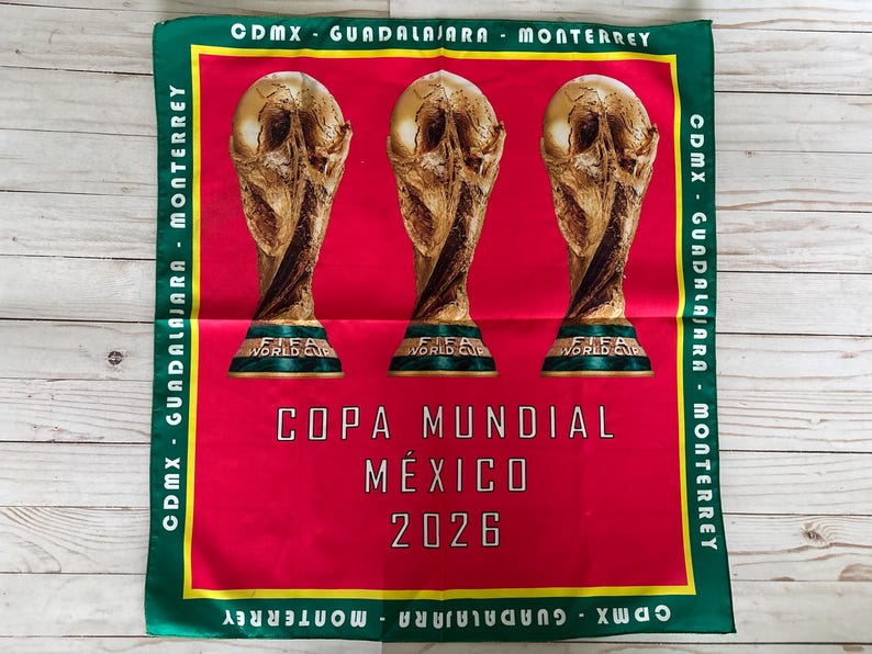 May include: A red and green square textile featuring three gold FIFA World Cup trophies. The text "COPA MUNDIAL M&Eacute;XICO 2026" is centered below the trophies. The border includes the text "CDMX - GUADALAJARA - MONTERREY".