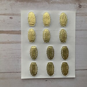 May include: A sheet of gold-coloured stickers featuring an image of the Virgin Mary. The stickers are arranged in three rows of four, with each sticker depicting the Virgin Mary in a similar pose.
