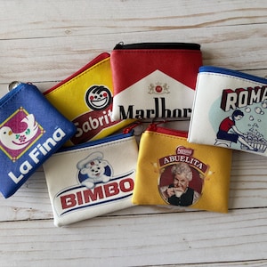 Può includere: Una collezione di piccole pochette con cerniera e vari loghi di marchi. Le pochette sono in diversi colori, tra cui blu, giallo, rosso e bianco. I loghi includono "La Fina", "Sabrit", "Marlboro", "Roma", "Bimbo" e "Abuelita".