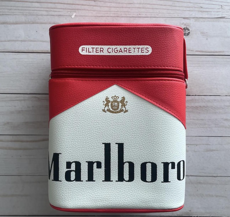 May include: A red, white, and black cigarette case with the word "Marlboro" in black lettering. The case has a zipper closure and the words "FILTER CIGARETTES" are printed on the top.