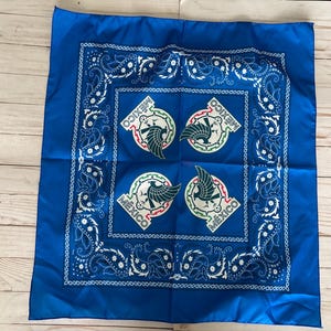 May include: A square, royal blue bandana with a white paisley border and four circular emblems featuring a green eagle and the word "MEXICO". The bandana is made of a smooth, possibly satin-like fabric.