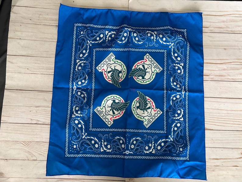 May include: A square, royal blue bandana with a white paisley border and four circular emblems featuring a green eagle and the word "MEXICO". The bandana is made of a smooth, possibly satin-like fabric.