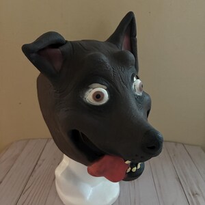 May include: A brown dog mask with a red tongue sticking out. The mask has large, round eyes and a toothy grin.