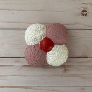 May include: A four-piece flower-shaped cake with white and pink frosting and a red cherry in the center.