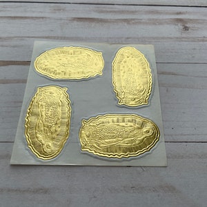 May include: Four gold foil stickers featuring an image of the Virgin Mary. The stickers are on a white sheet.