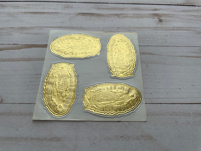 May include: Four gold foil stickers featuring an image of the Virgin Mary. The stickers are on a white sheet.