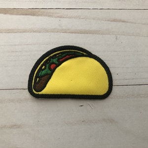 Op de afbeelding: Een geborduurde strijk-op patch in de vorm van een taco met bruine, rode en groene vulling.