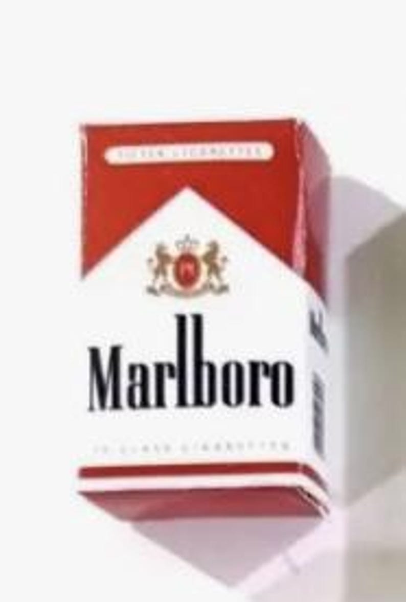 May include: A pack of Marlboro cigarettes, featuring a white background with the brand name in bold black letters. The top and sides are red, with the Marlboro logo and text. The pack is rectangular and stands upright.