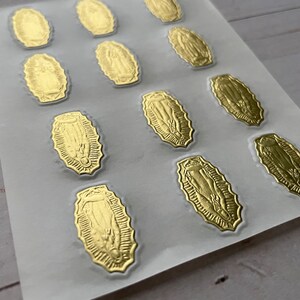 May include: A sheet of gold foil stickers featuring an image of the Virgin Mary. The stickers are oval shaped and have a detailed design.