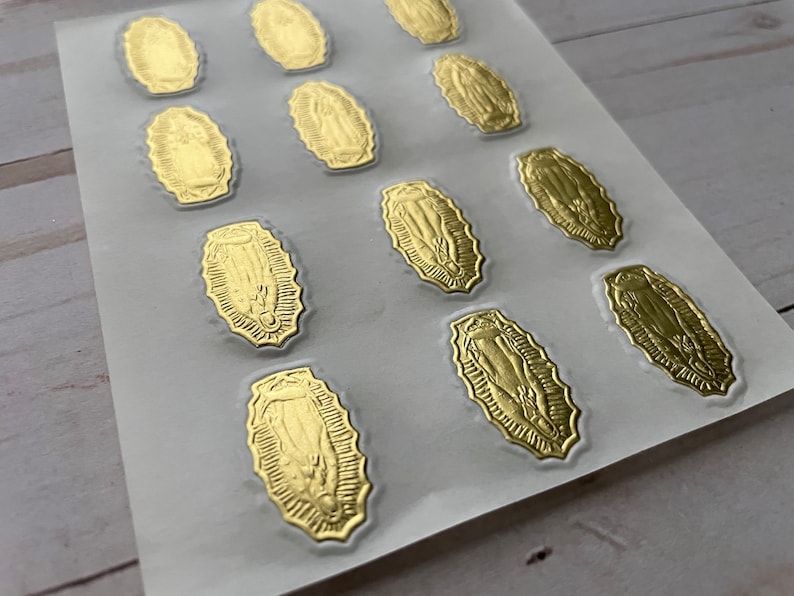 May include: A sheet of gold foil stickers featuring an image of the Virgin Mary. The stickers are oval shaped and have a detailed design.